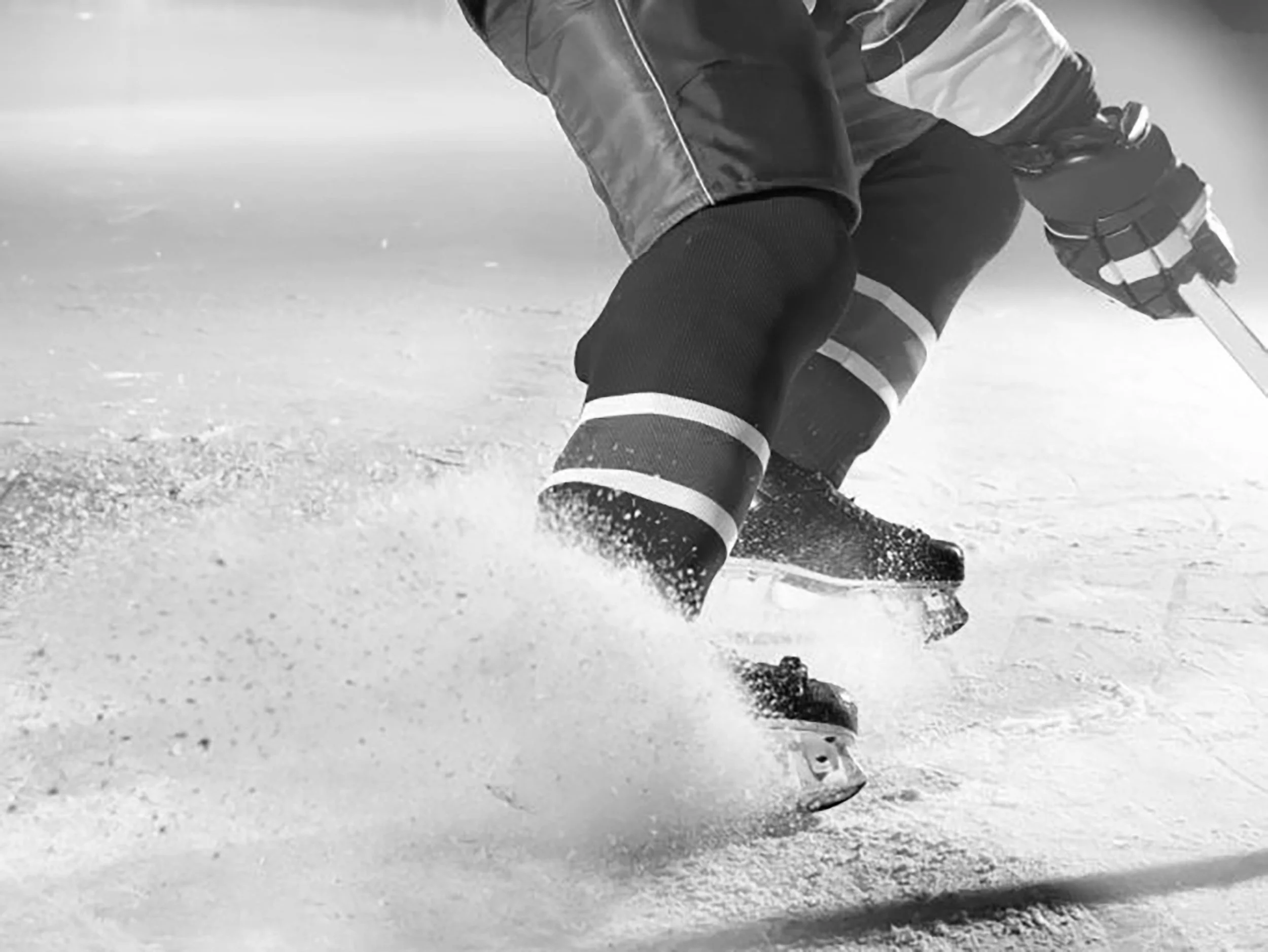 Close-up of a skier sliding on snow, wearing ski boots, pants, and a jacket, captured in black and white.