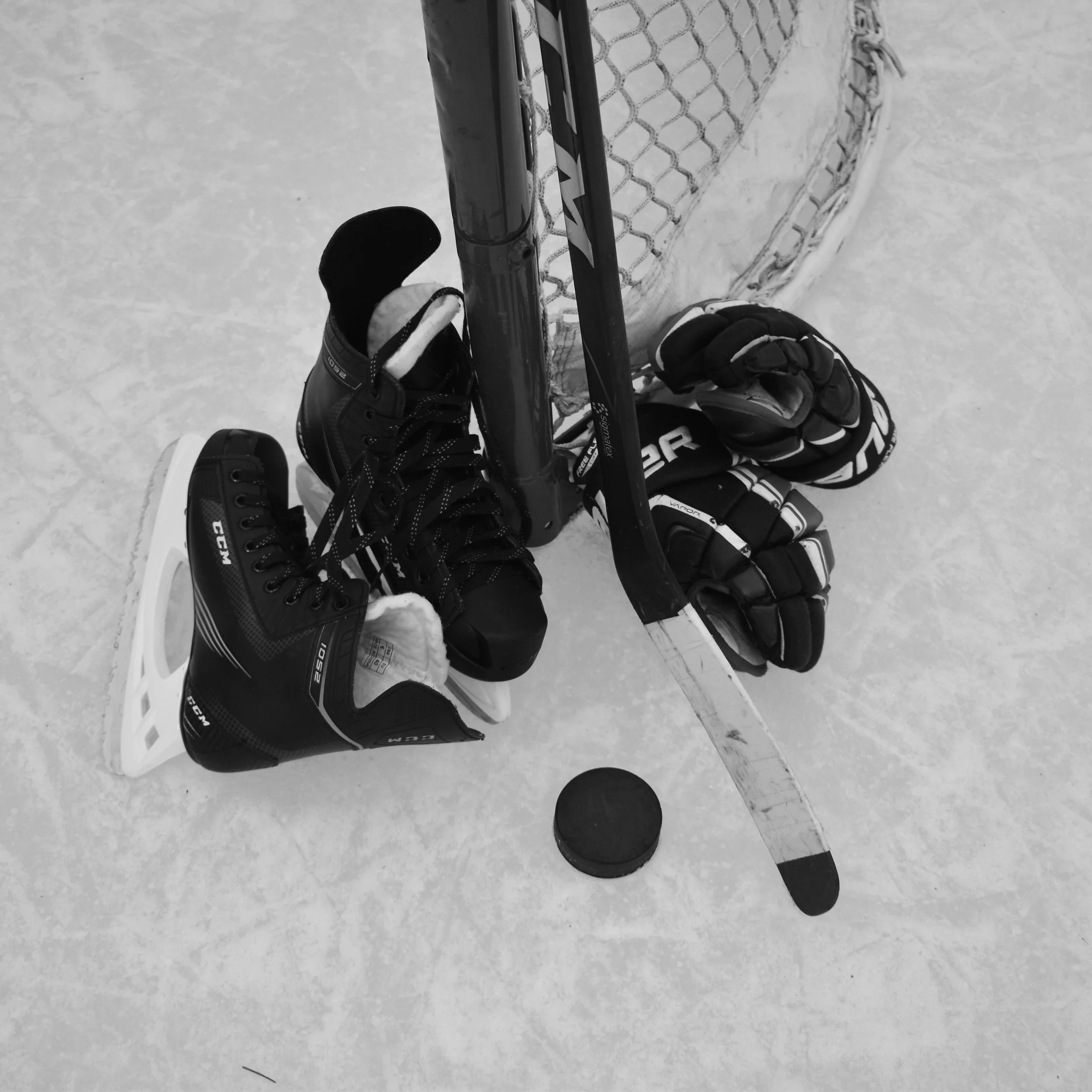 Hockey equipment including skates, gloves, a hockey stick, a puck, and a hockey net on the ice.
