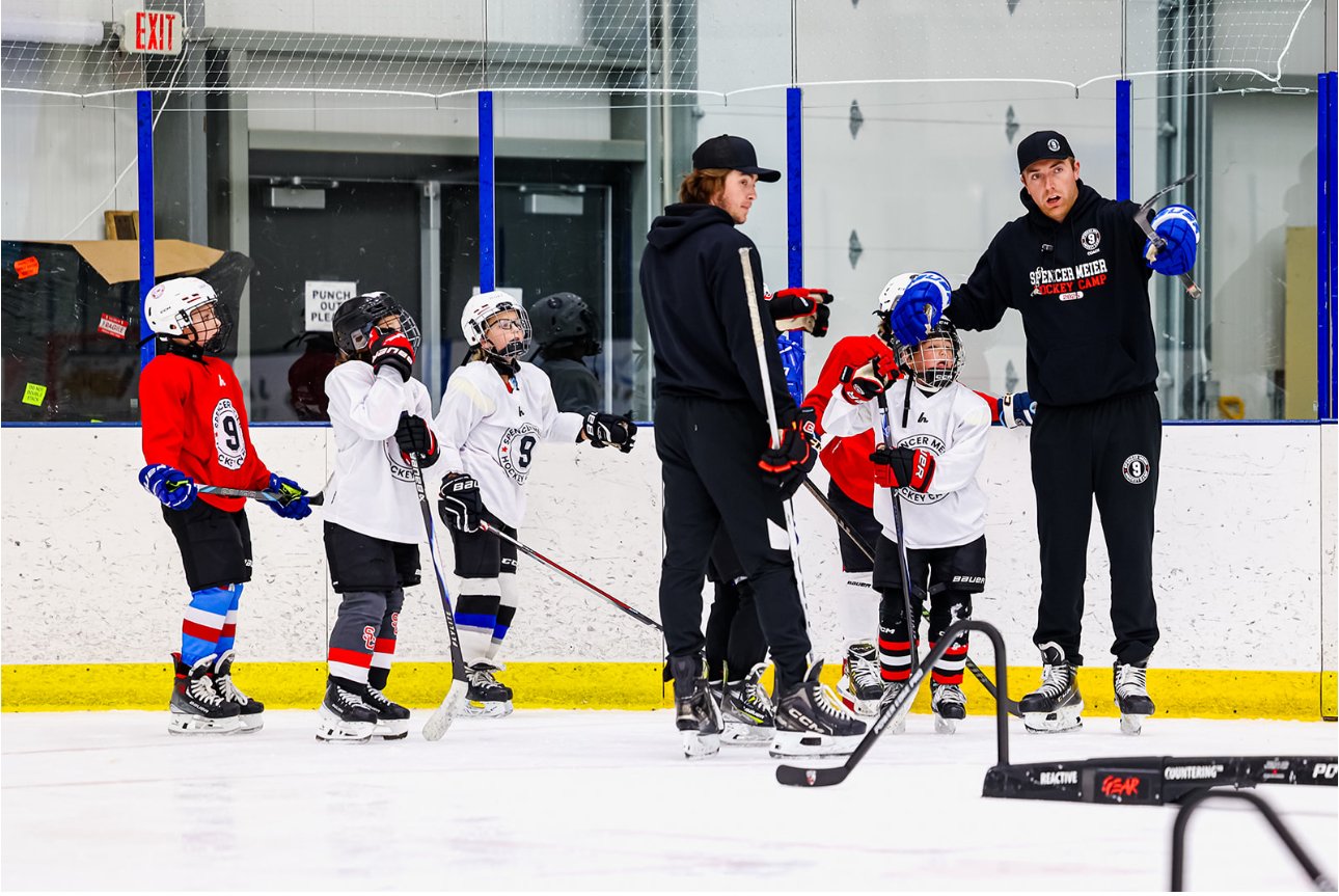 Hockey coaches instruct young players on the ice at an indoor rink during practice.