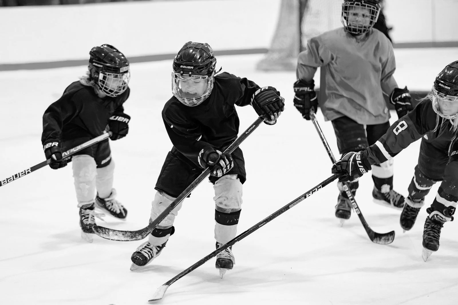 Young hockey players practicing on ice rink, wearing helmets and protective gear.