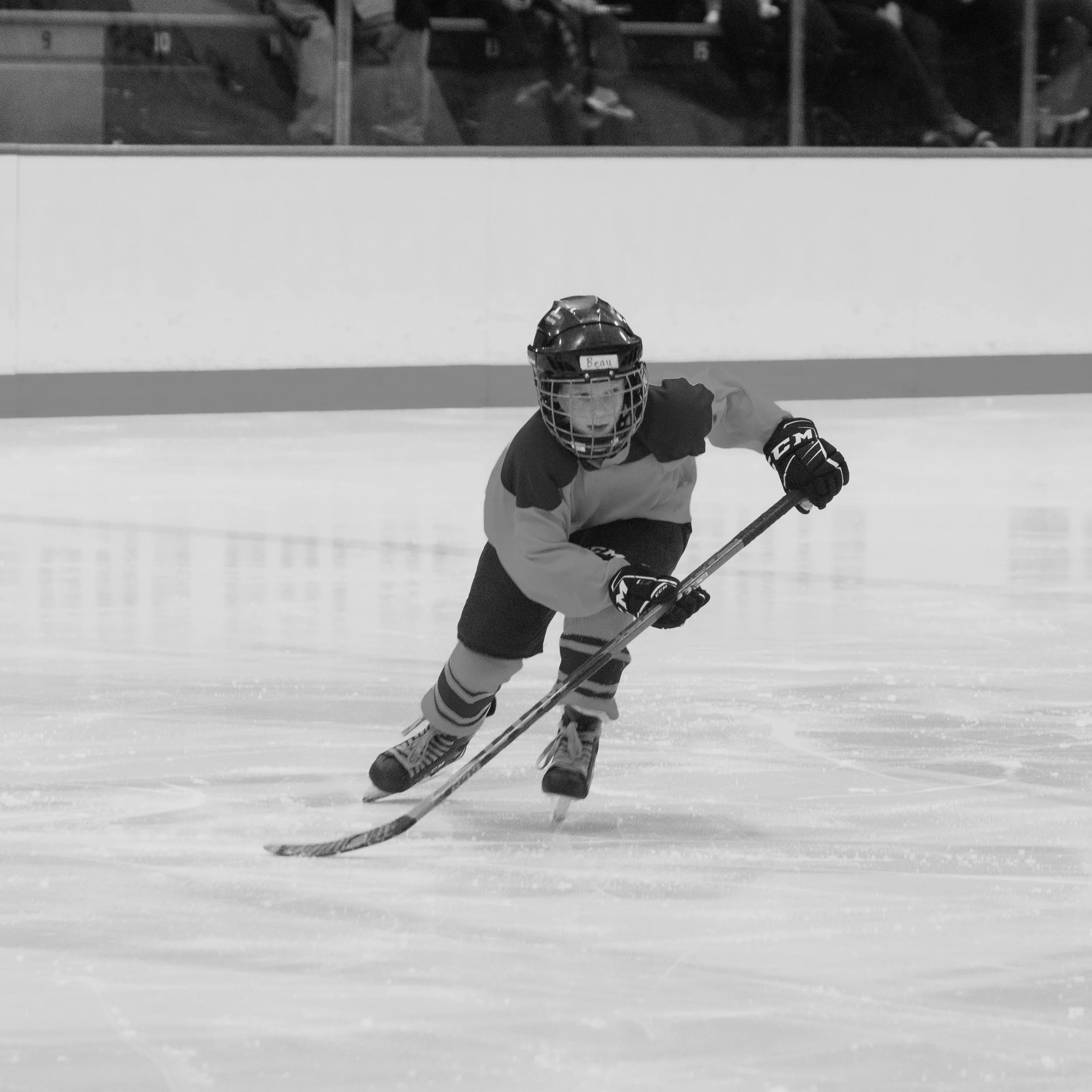A young hockey player in a helmet and jersey shoots the puck on ice in an indoor rink.