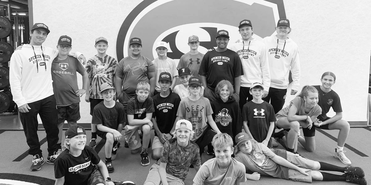 A group of children and coaches in a gym, posing together for a photo, with some children kneeling or sitting in front and others standing behind them.