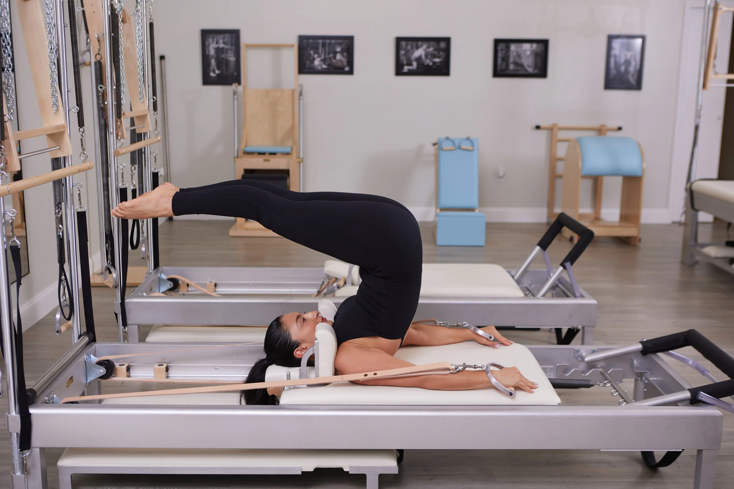 Woman in aerobics studio performing Pilates exercise on reformer machine.