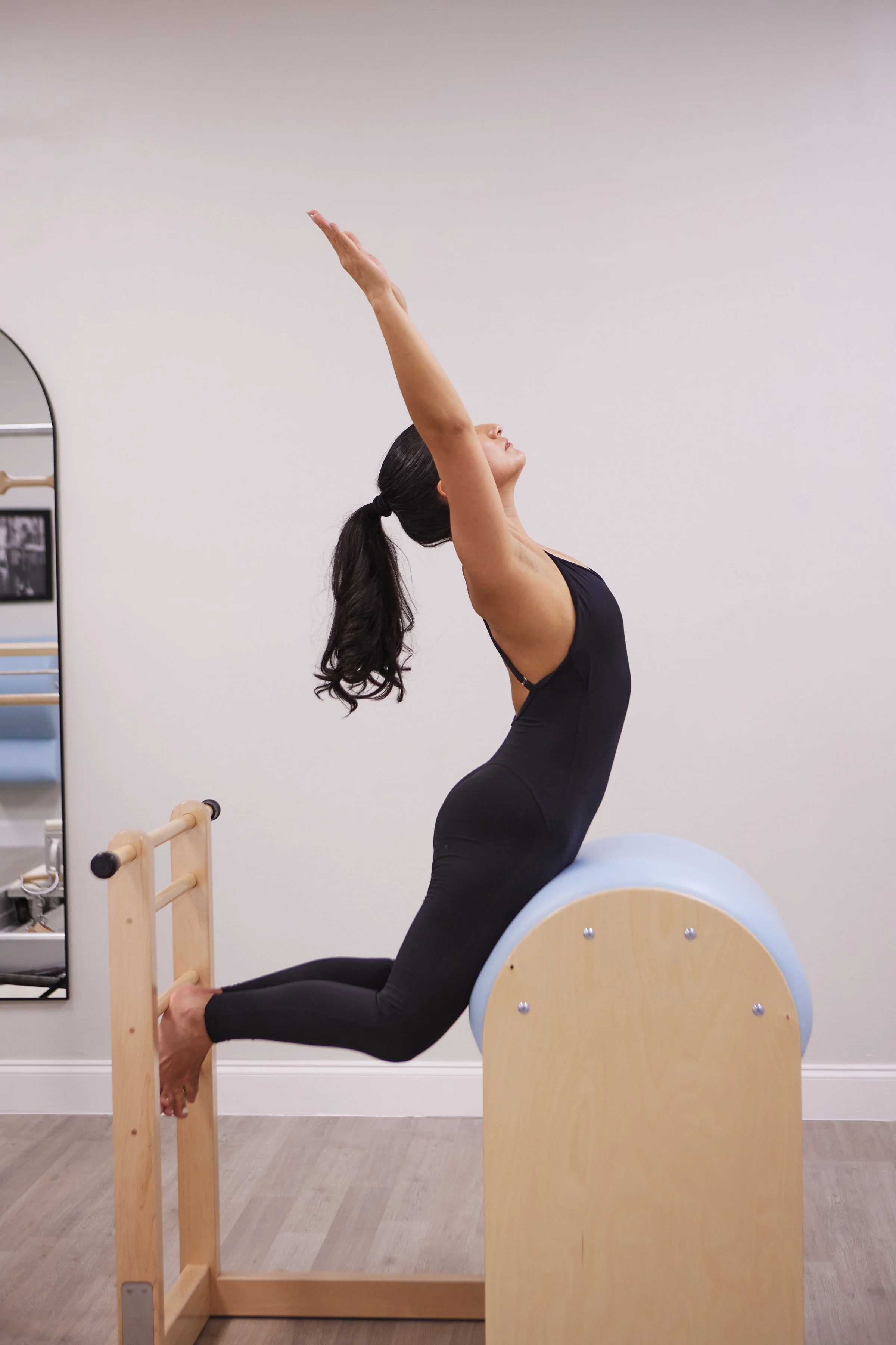 Woman doing a backbend stretch on pilates equipment with her arms extended upward.
