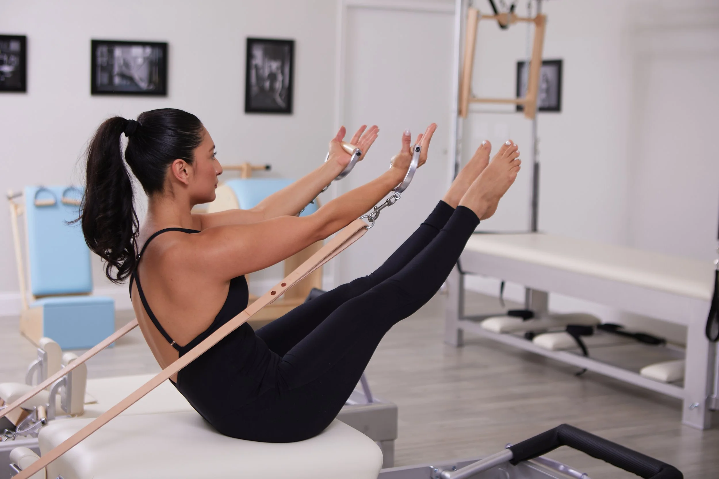 Woman in black workout clothes doing Pilates with a walker and resistance bands in a rehab or physical therapy clinic.
