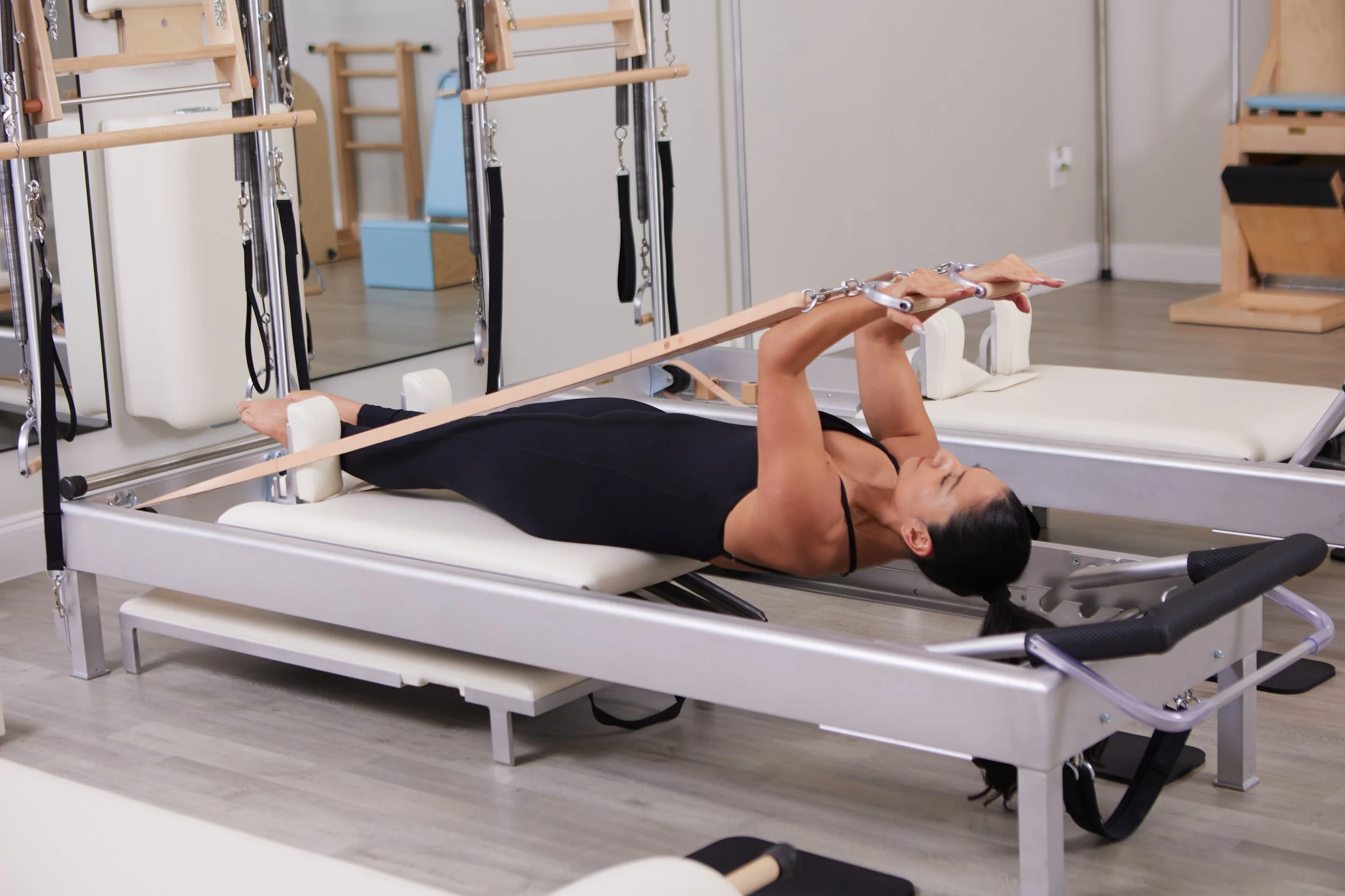 Woman performing leg exercises on a Pilates reformer machine in a fitness studio