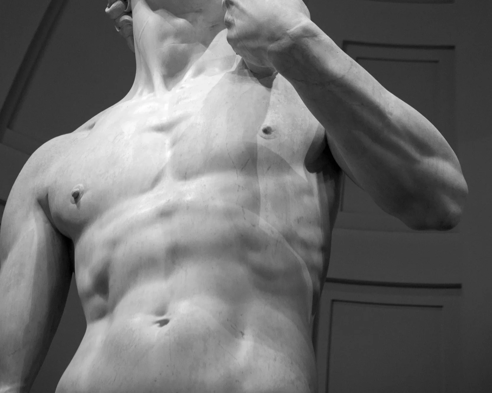 Close-up view of a classical marble statue of a male torso, highlighting the chest, abdomen, and part of an arm.