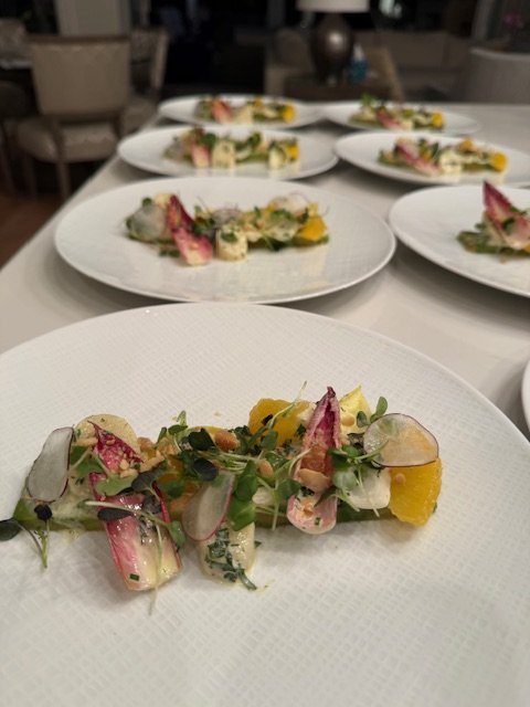 Multiple plates of gourmet salad with microgreens, radishes, yellow flowers, and mixed vegetables on a white table in a dining setting.