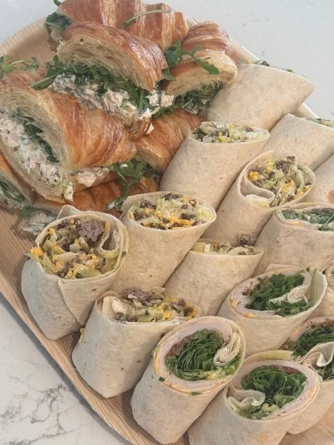 Assorted wraps and croissant sandwiches on a wooden platter.