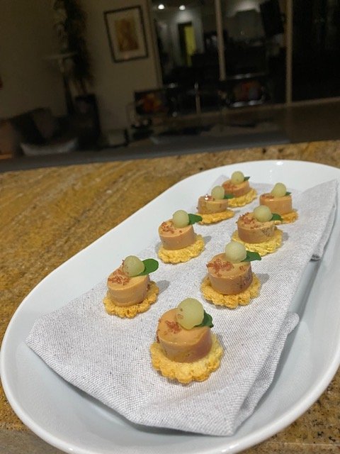 Miniature desserts on a white oval platter with a paper napkin, each with a round base, a small topping, and a green garnish, set on a kitchen countertop.