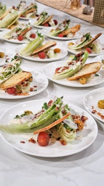 Multiple white plates with garnish salads containing lettuce, cherry tomatoes, radishes, croutons, and dressing, arranged on a white table.