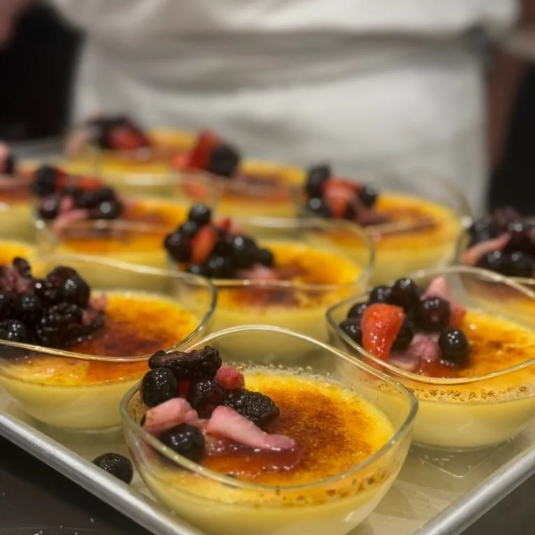 Several bowls of crème brûlée topped with mixed berries on a tray.