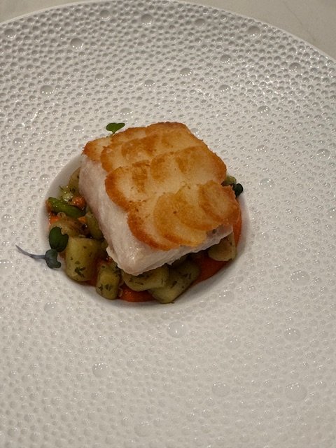 A piece of crispy, golden brown fish fillet on a bed of diced vegetables, served in a white bowl.