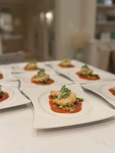 Multiple white plates with shrimp appetizers on a countertop in a kitchen.