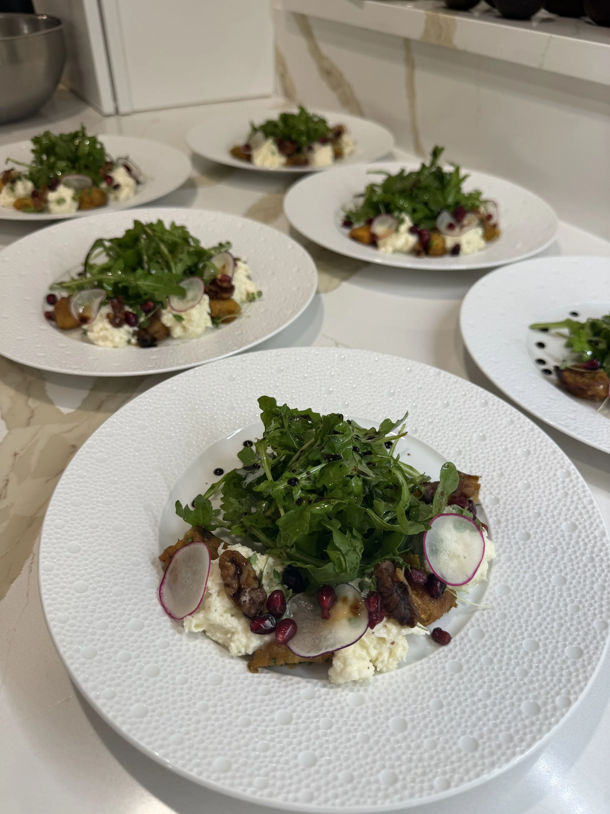 A white textured plate with a salad consisting of greens, radish slices, pomegranate seeds, and other vegetables, placed on a white marble surface.