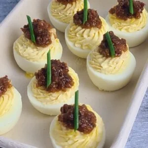 Deviled eggs topped with chili and green garnish on a white serving tray.