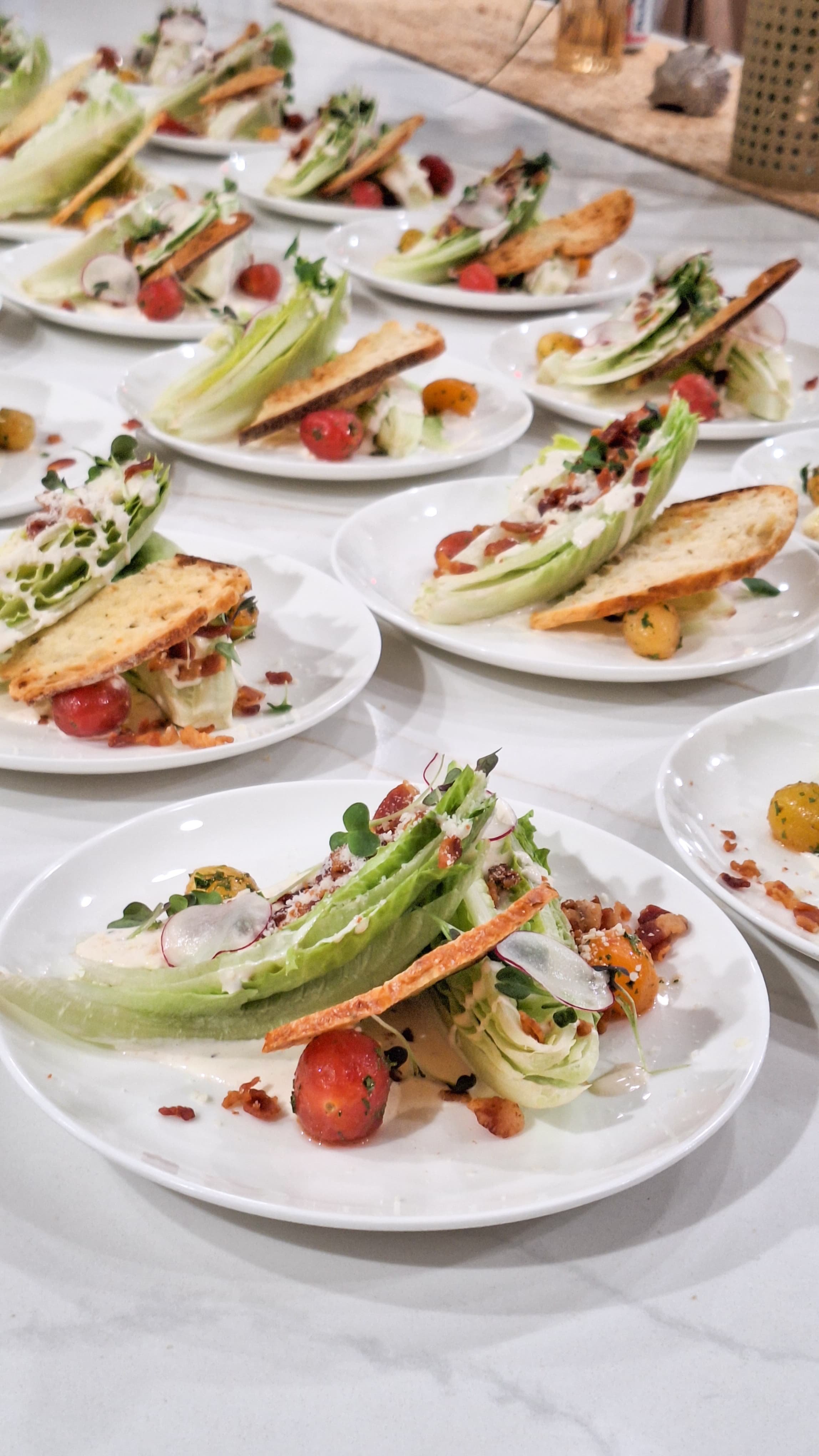 Multiple white plates with salad and bread tostadas, cherry tomatoes, and greens, arranged on a white table
