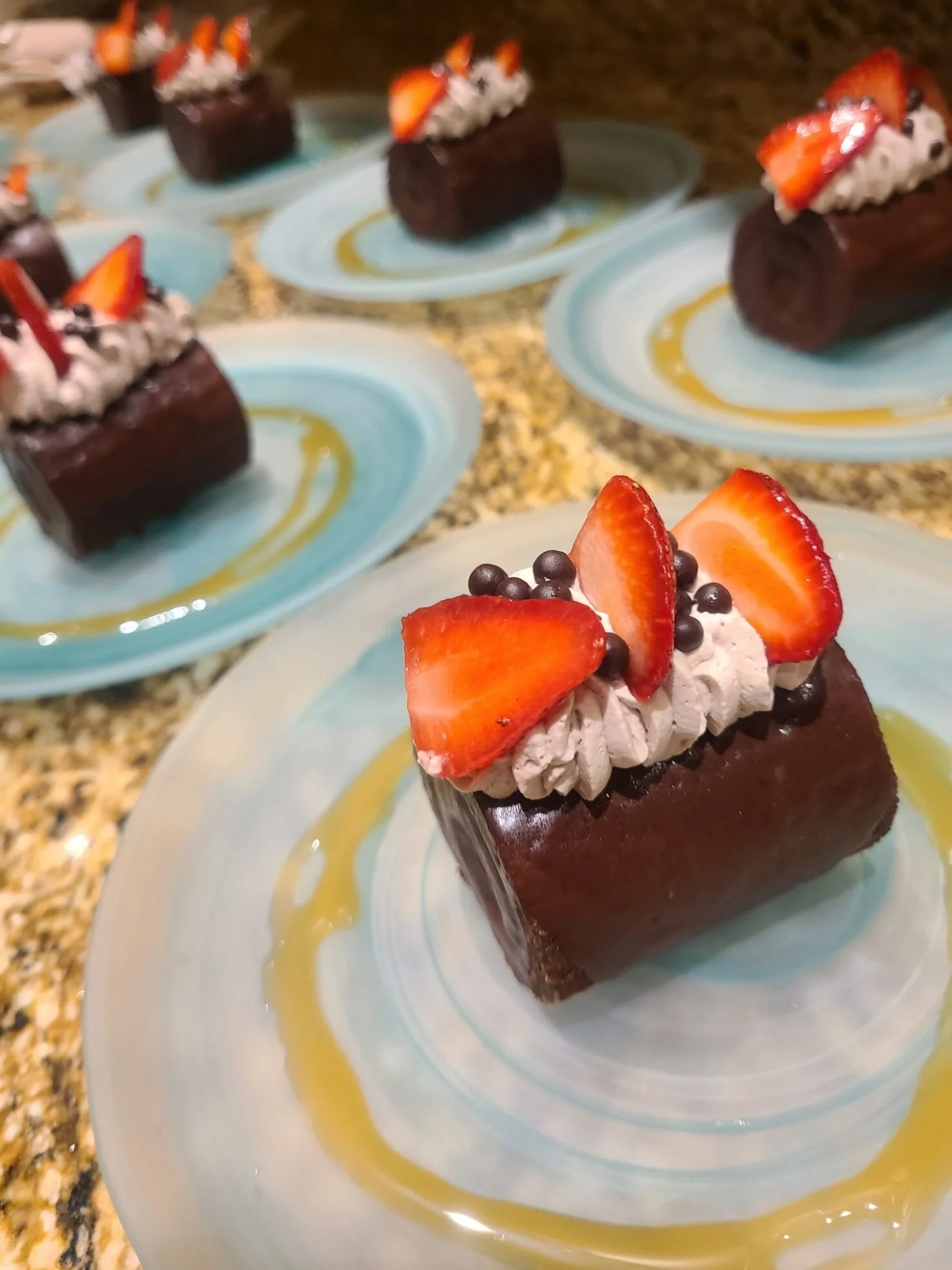 Chocolate dessert topped with whipped cream, sliced strawberries, and chocolate pearls, served on a decorative plate with a drizzle of caramel sauce.