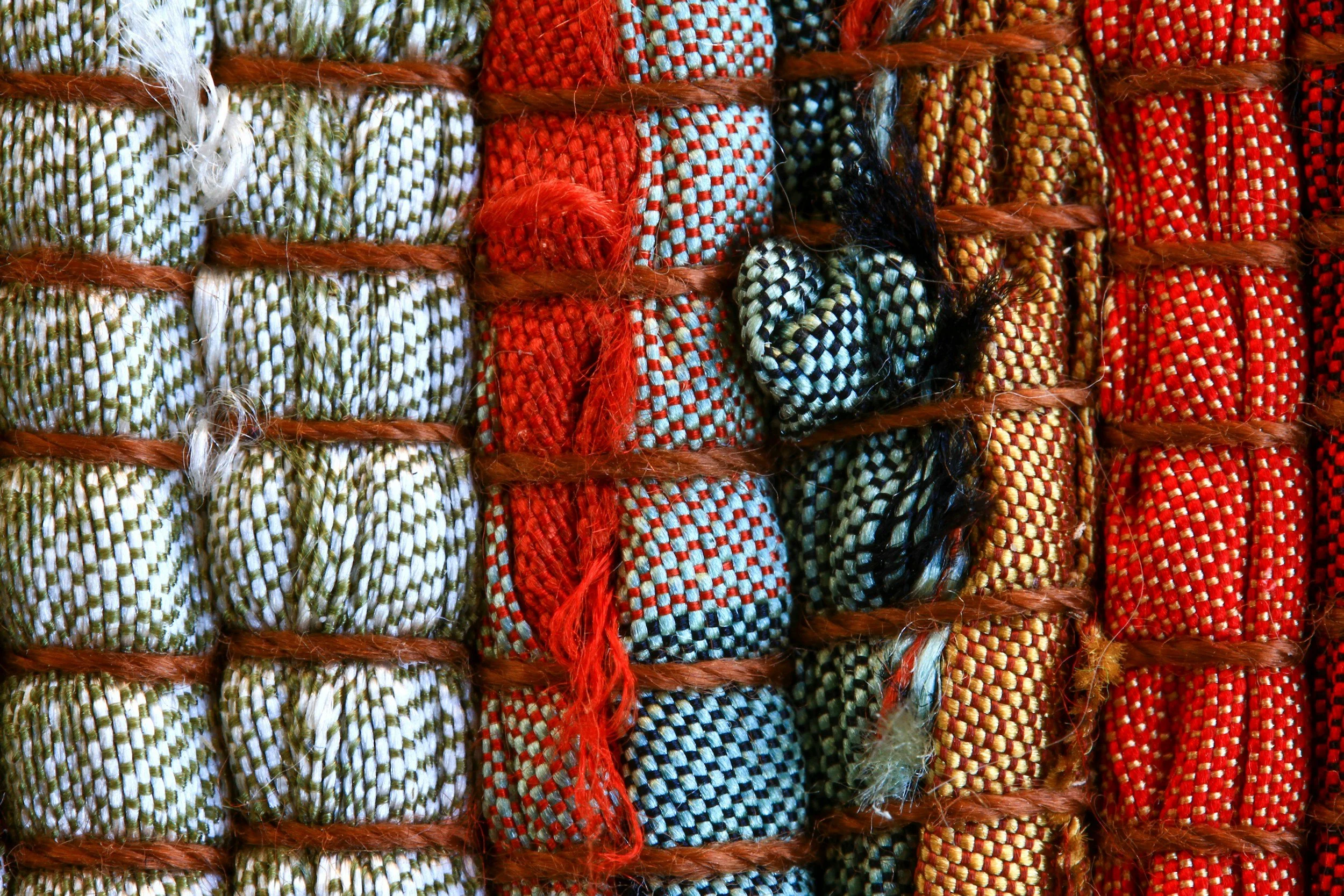 Close-up of colorful woven ropes arranged in vertical stripes, with each stripe a different detailed pattern and color, including white, green, red, black, and gold.
