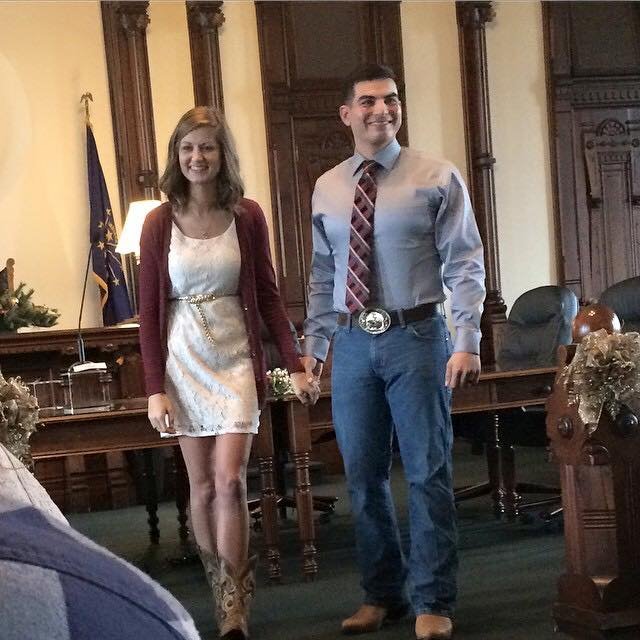 Young man and woman standing in a formal room, holding hands, smiling.