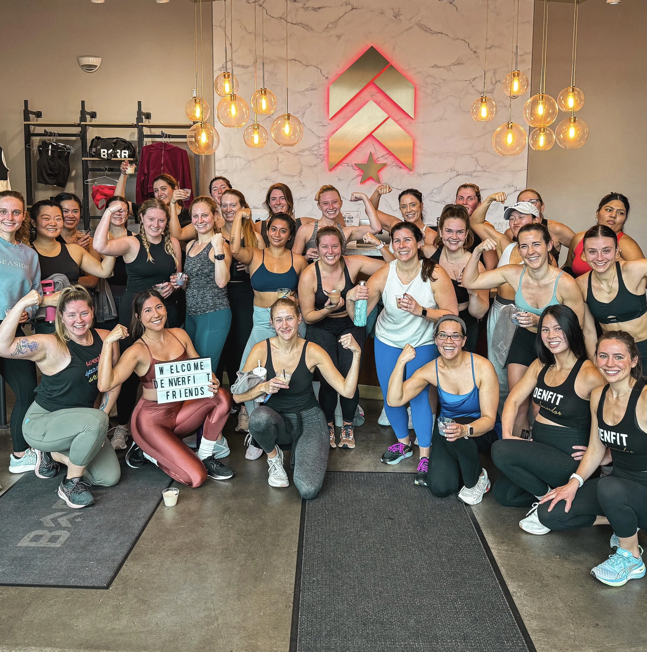 Group of women posing at a fitness gym, some flexing muscles and smiling.