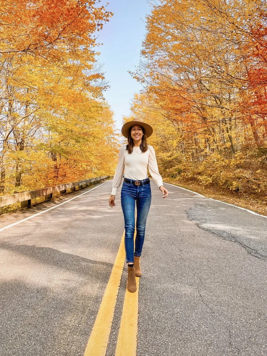 woman standing in middle of road with fall foilage