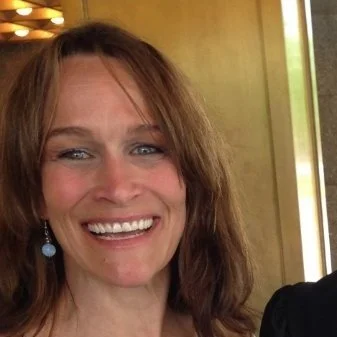 Close-up of a woman with light skin, brown hair, blue eyes, and earrings, smiling.