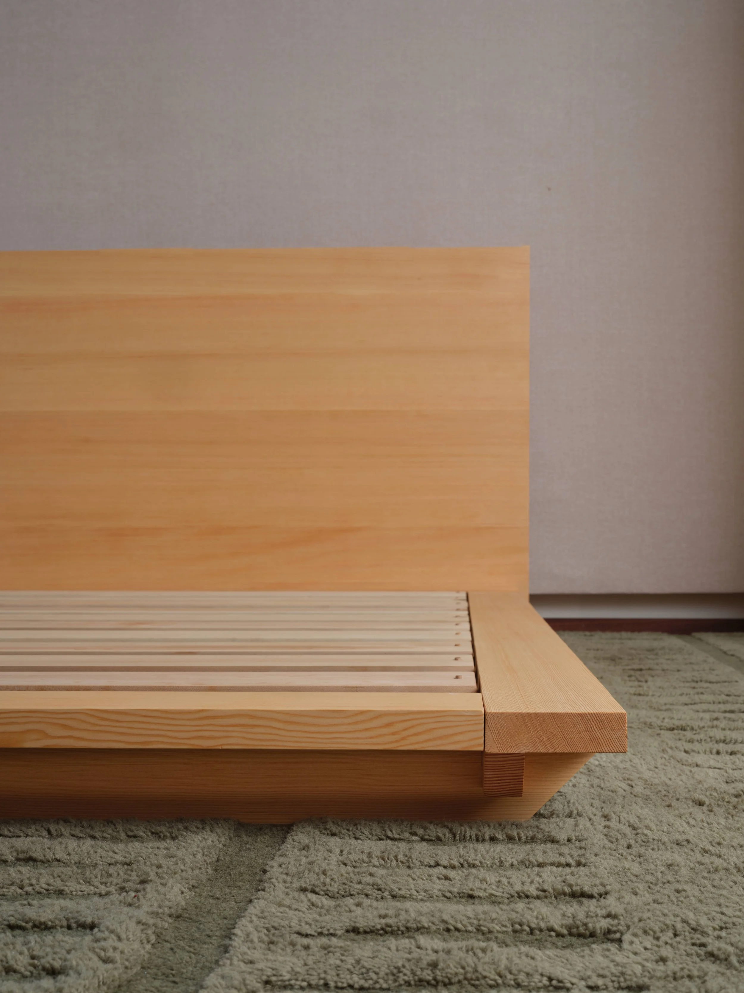 Wooden bed frame with a headboard, placed on a concrete floor against a plain white wall.