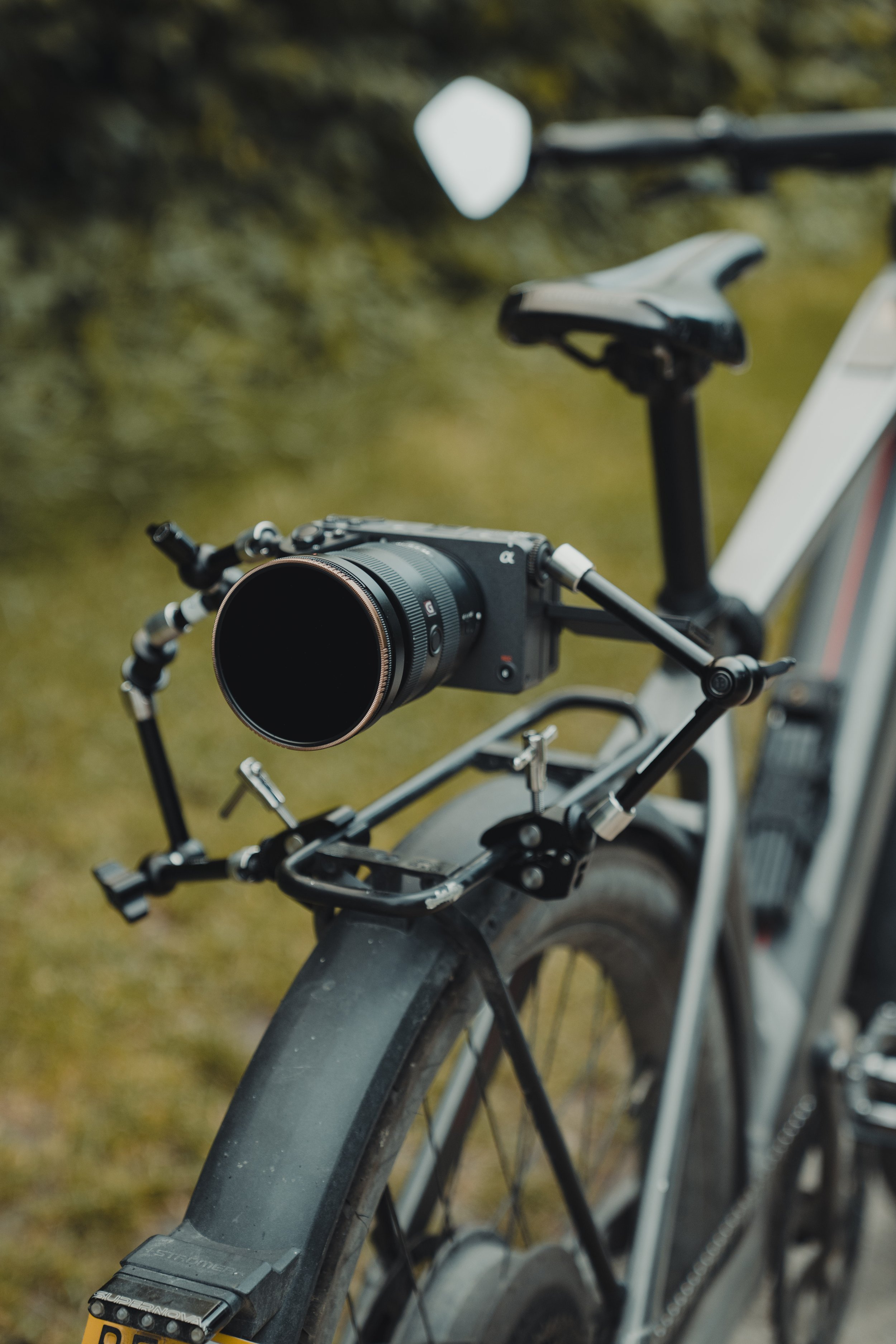 Nahaufnahme eines schwarzen Fahrrads mit GPS- oder Action-Kamera am Lenker, vor einer grünen, unscharfen Naturkulisse.
