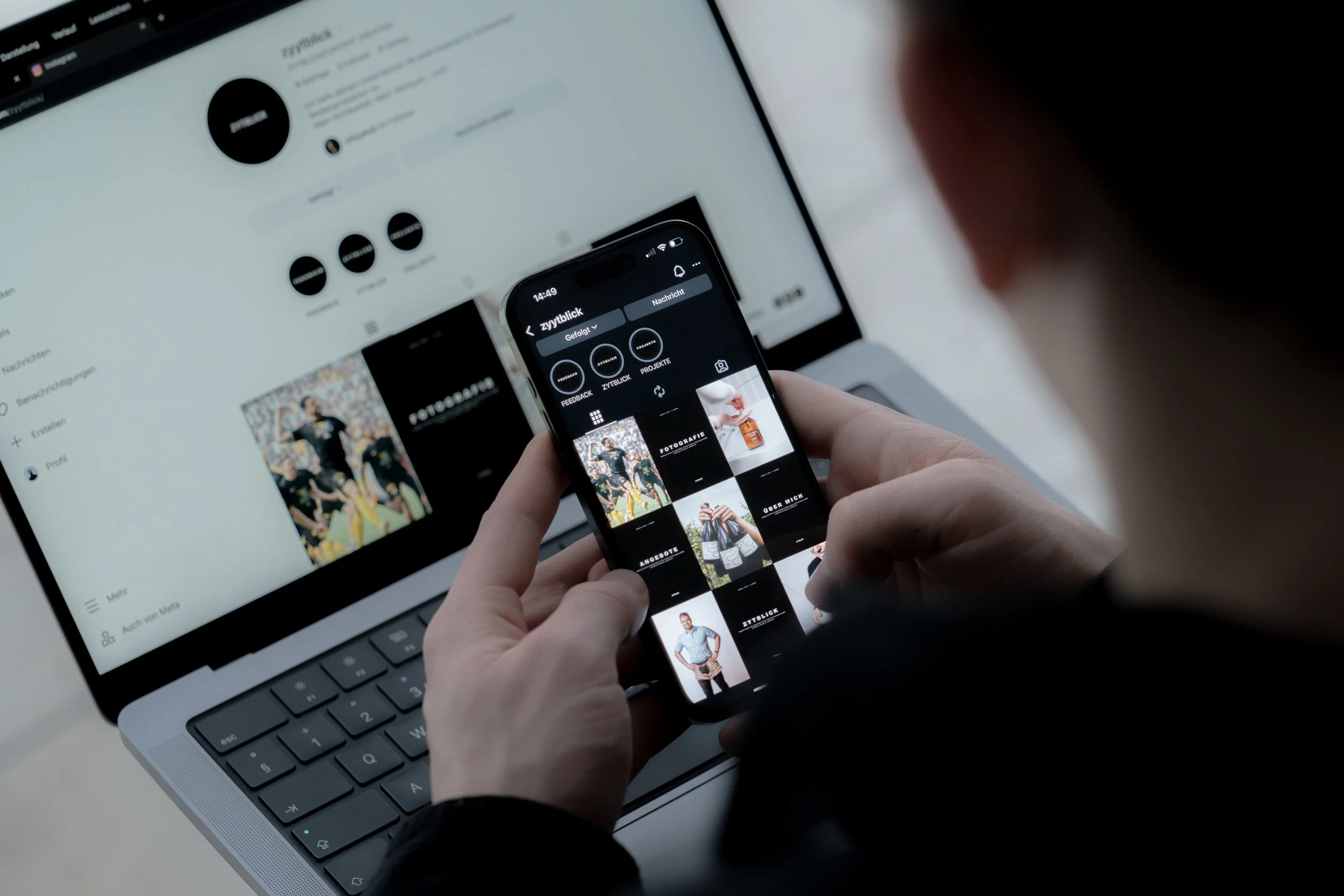 Hand hält Smartphone mit Instagram-Profil, Laptop im Hintergrund zeigt Instagram-Seite.