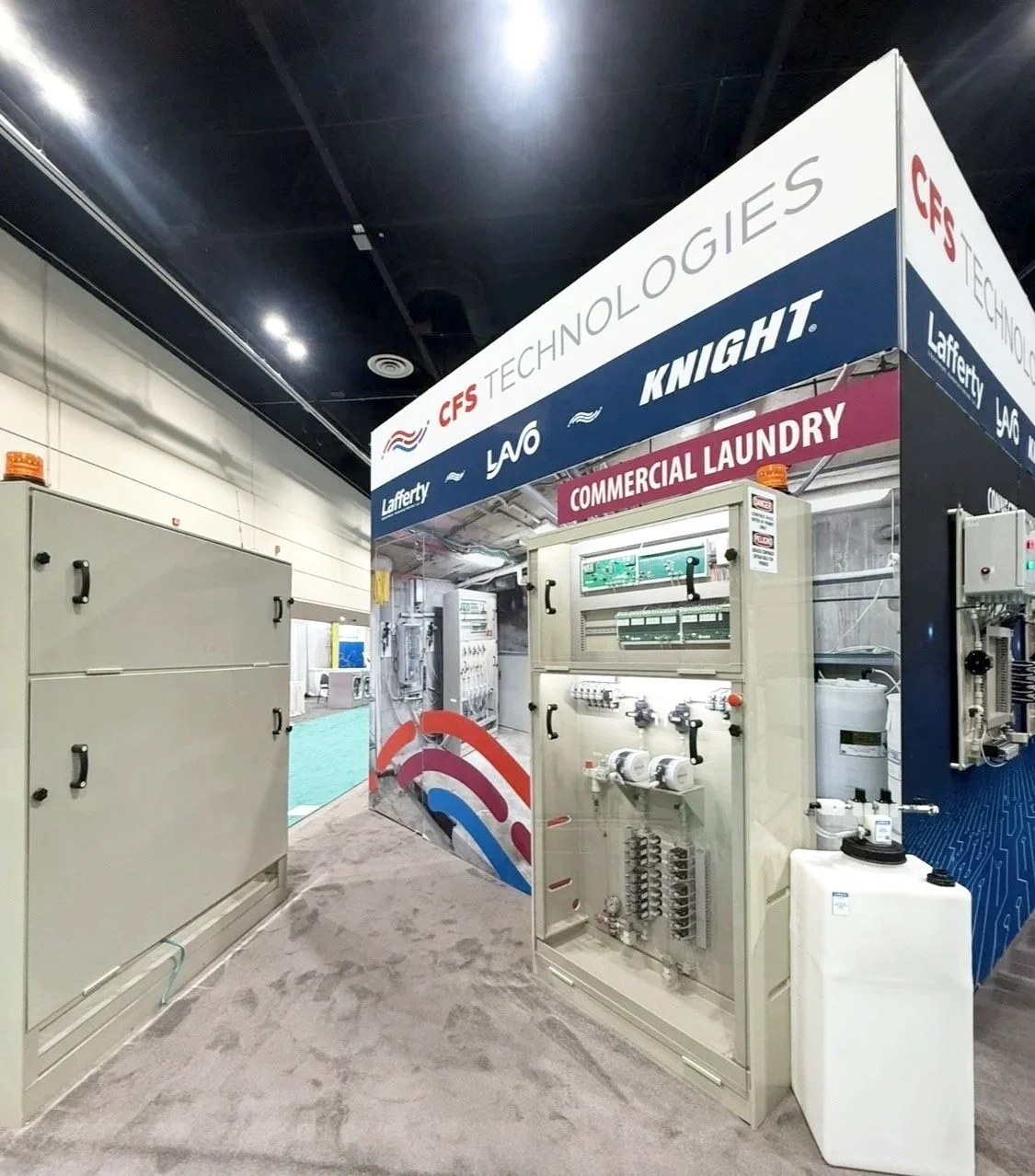 Exhibit booth for CFS Technologies at a trade show, showcasing commercial laundry equipment and systems.