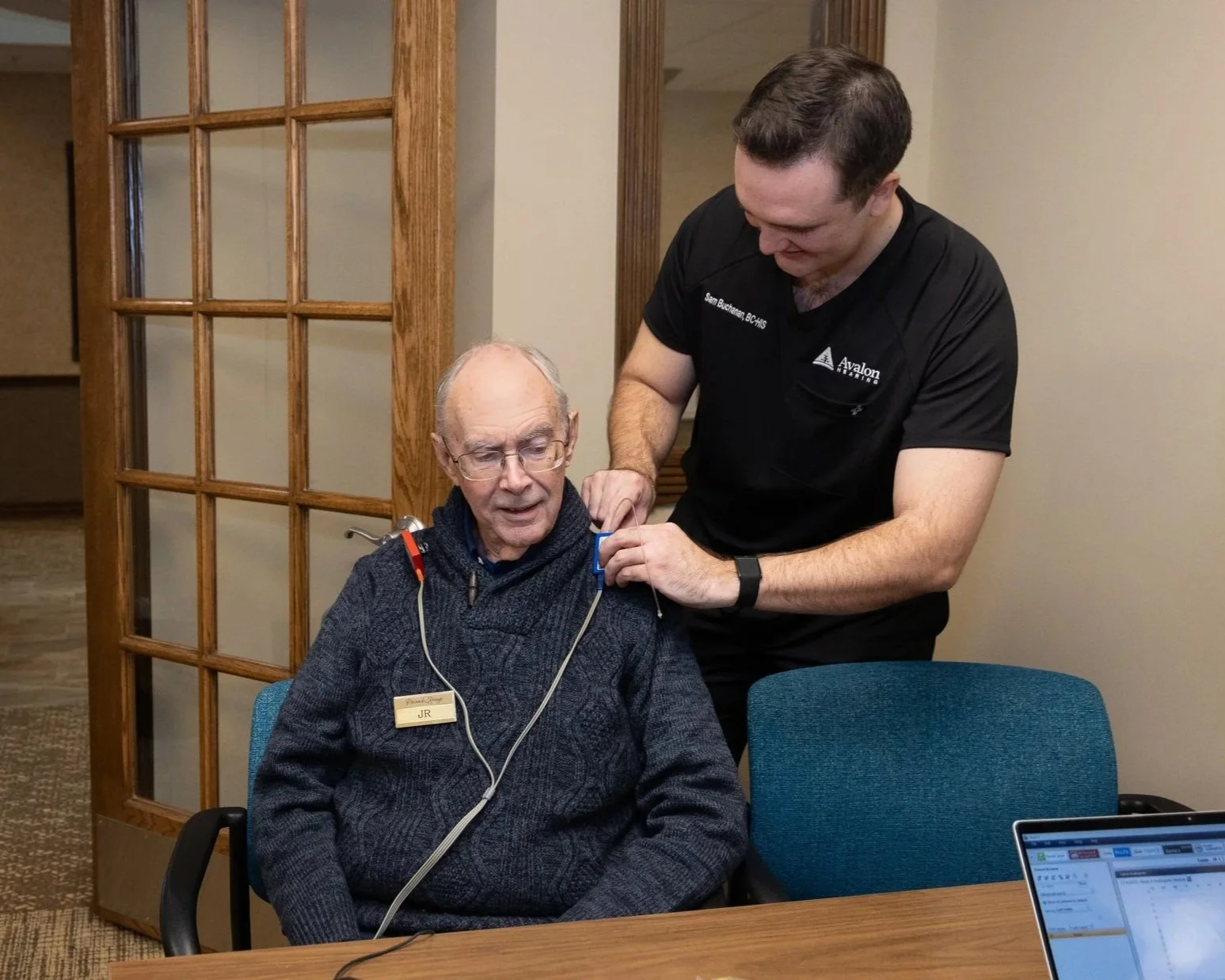 A healthcare professional fits a patient with a medical device using wires and electrodes on his chest in a clinic or office setting.