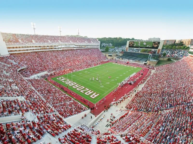 Aerial view of a packed football stadium with players on the field and a large scoreboard displaying the game.