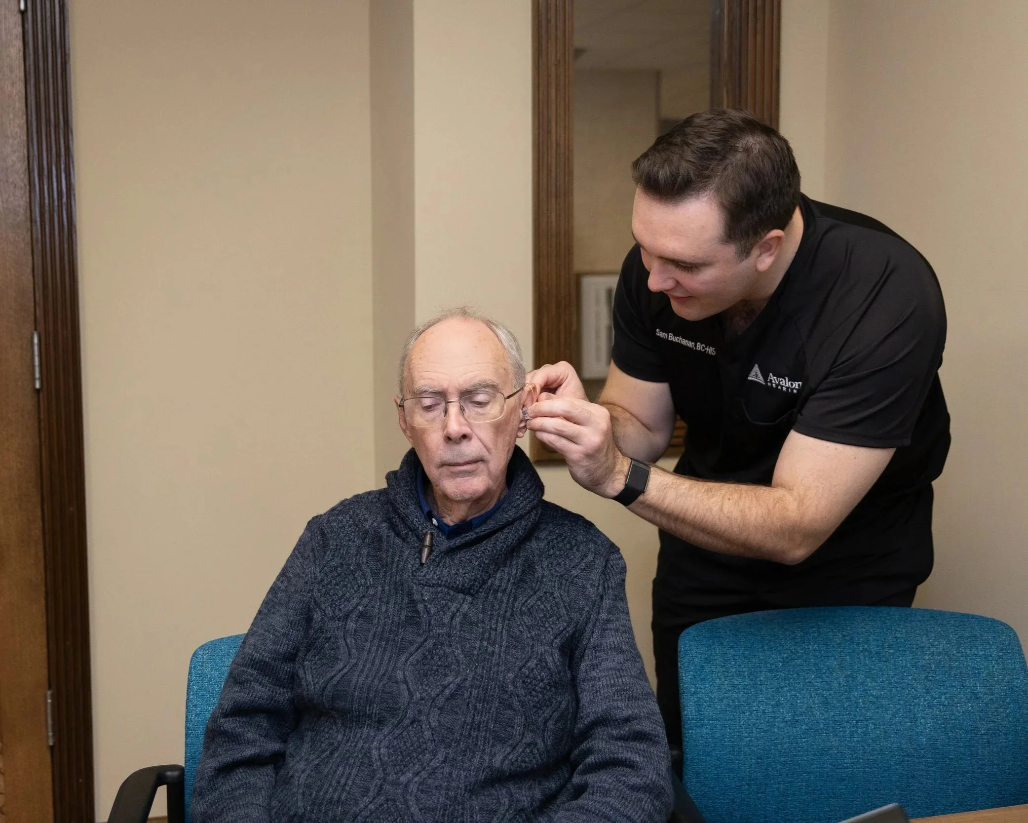 A healthcare professional assisting an elderly man by fitting an earpiece.