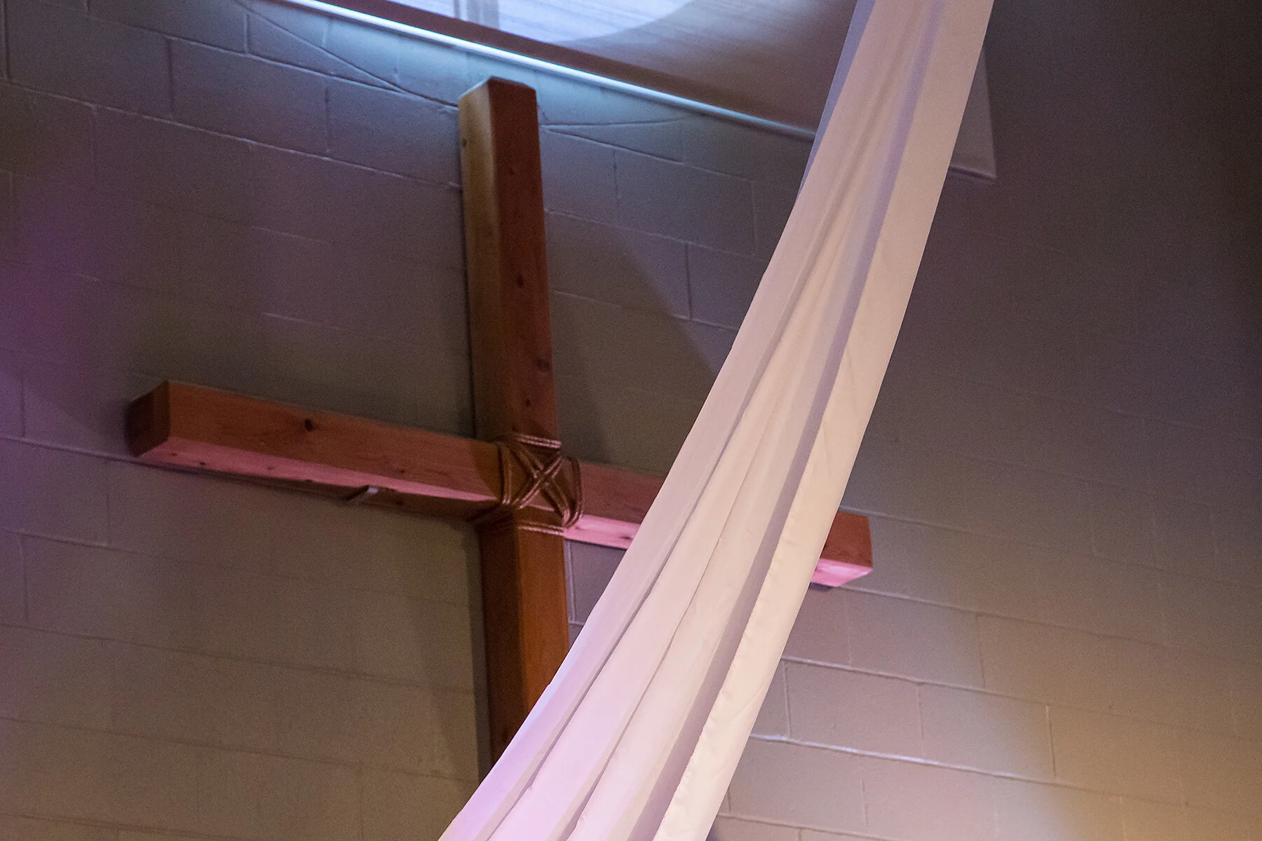 Wooden cross-shaped structure with a diagonal white beam leaning against it, mounted on a tiled wall.
