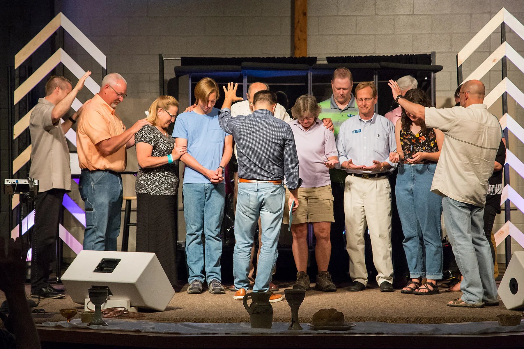 A group of people standing on a stage with their heads bowed and hands raised, participating in a prayer or spiritual moment during a religious gathering.