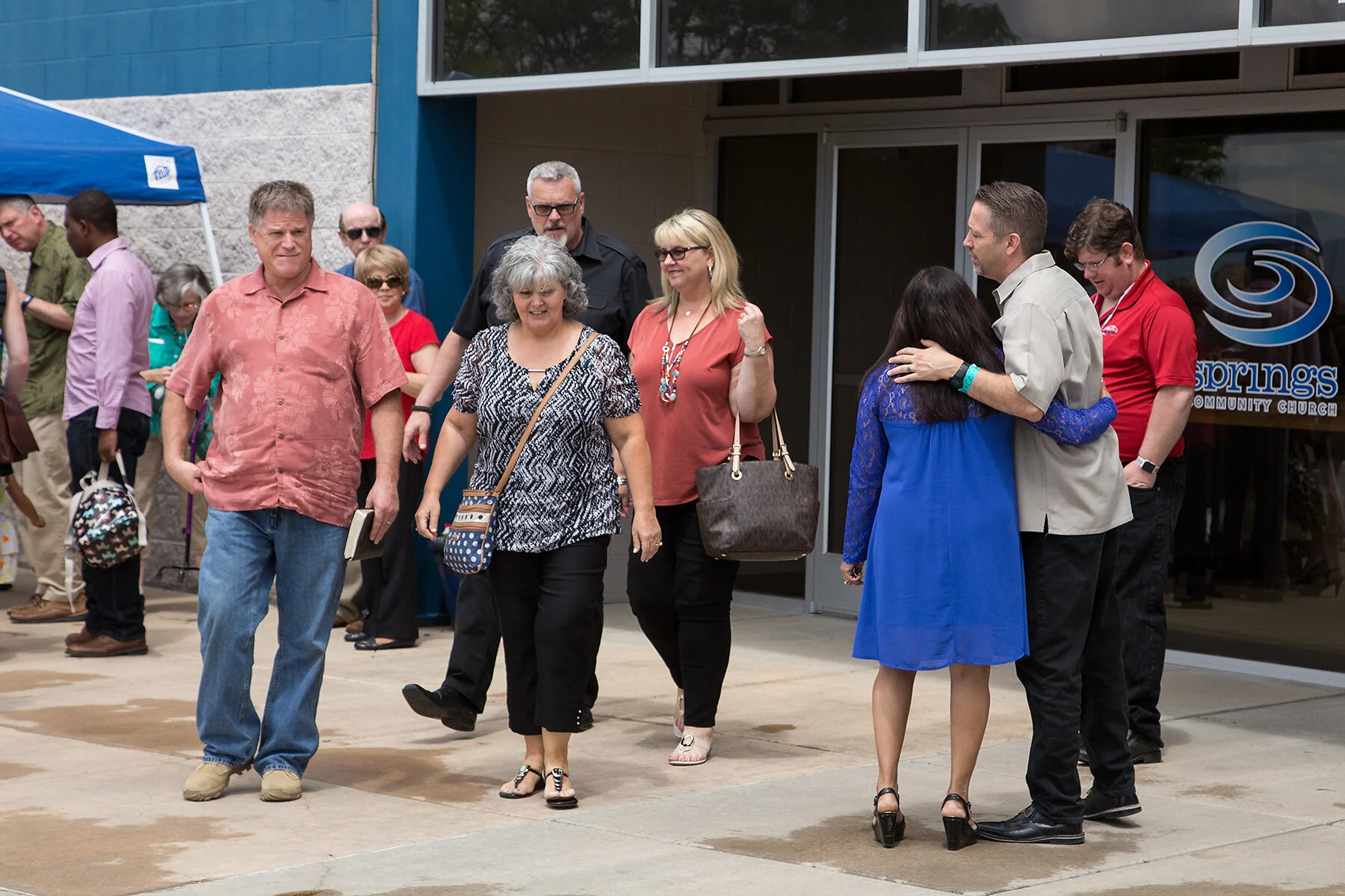 People standing and talking outside of a community church building with a sign that says 'Spring Community Church'.