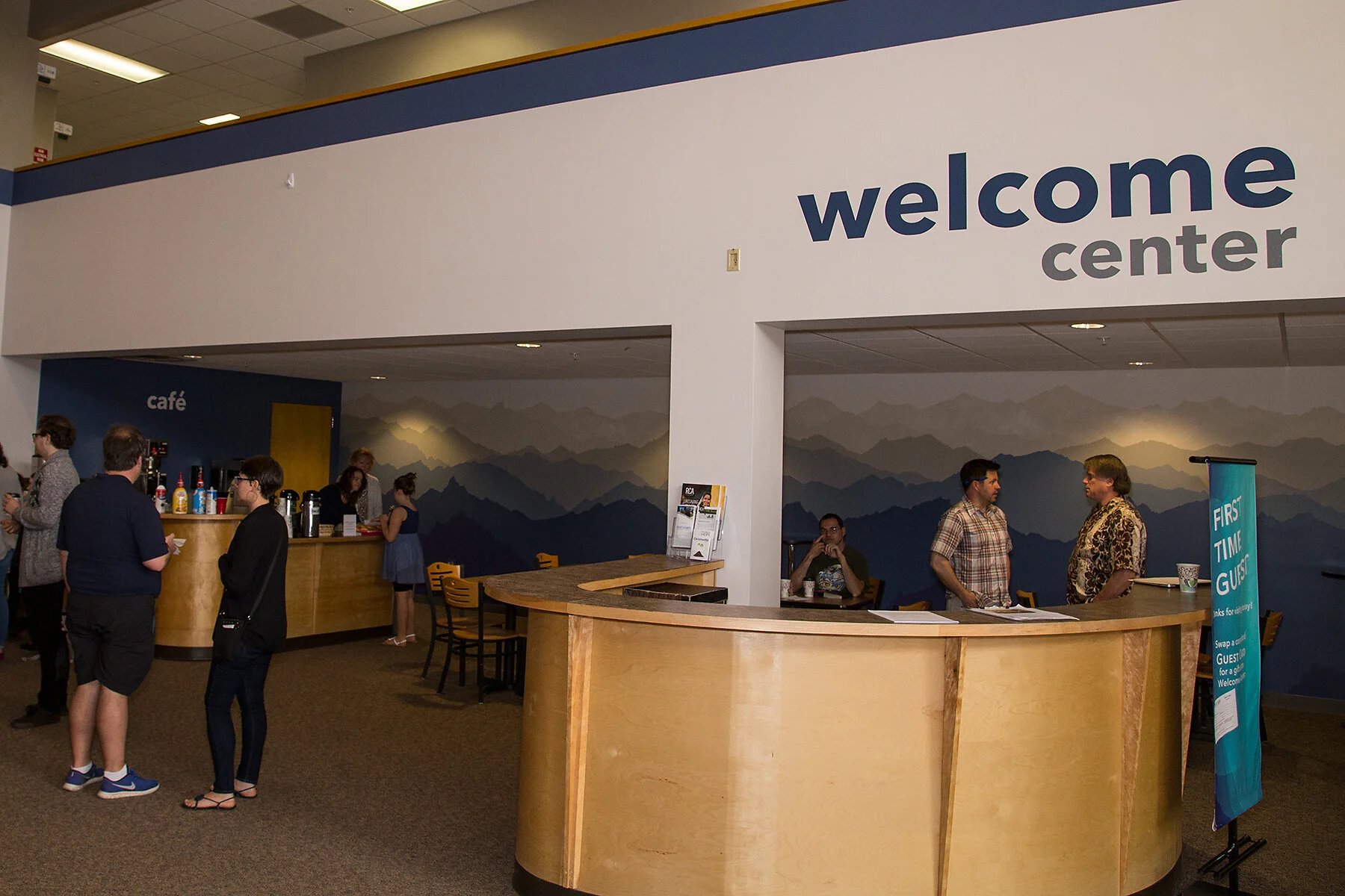 People at a check-in or reception desk in a welcome center with a mountain mural on the wall behind them.