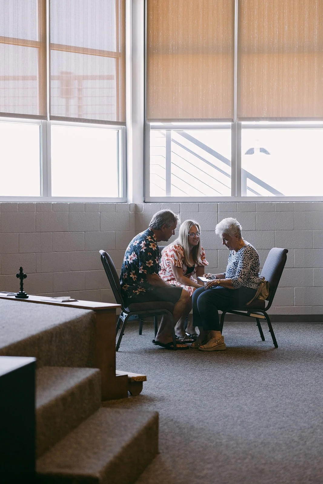 A man and a woman sit across from each other at a table, holding hands with their arms extended, over a Bible and an open book. Two cups of coffee are on the table.