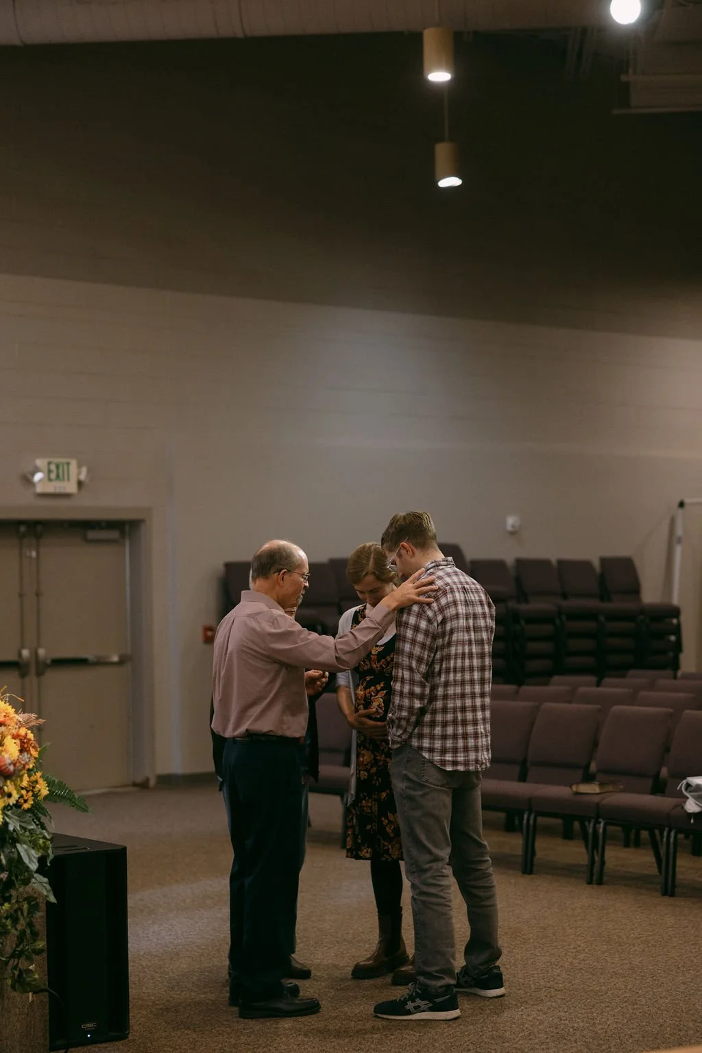 A family praying together in a church, with an older man, a woman, and a young man kneeling with their heads bowed and hands clasped.