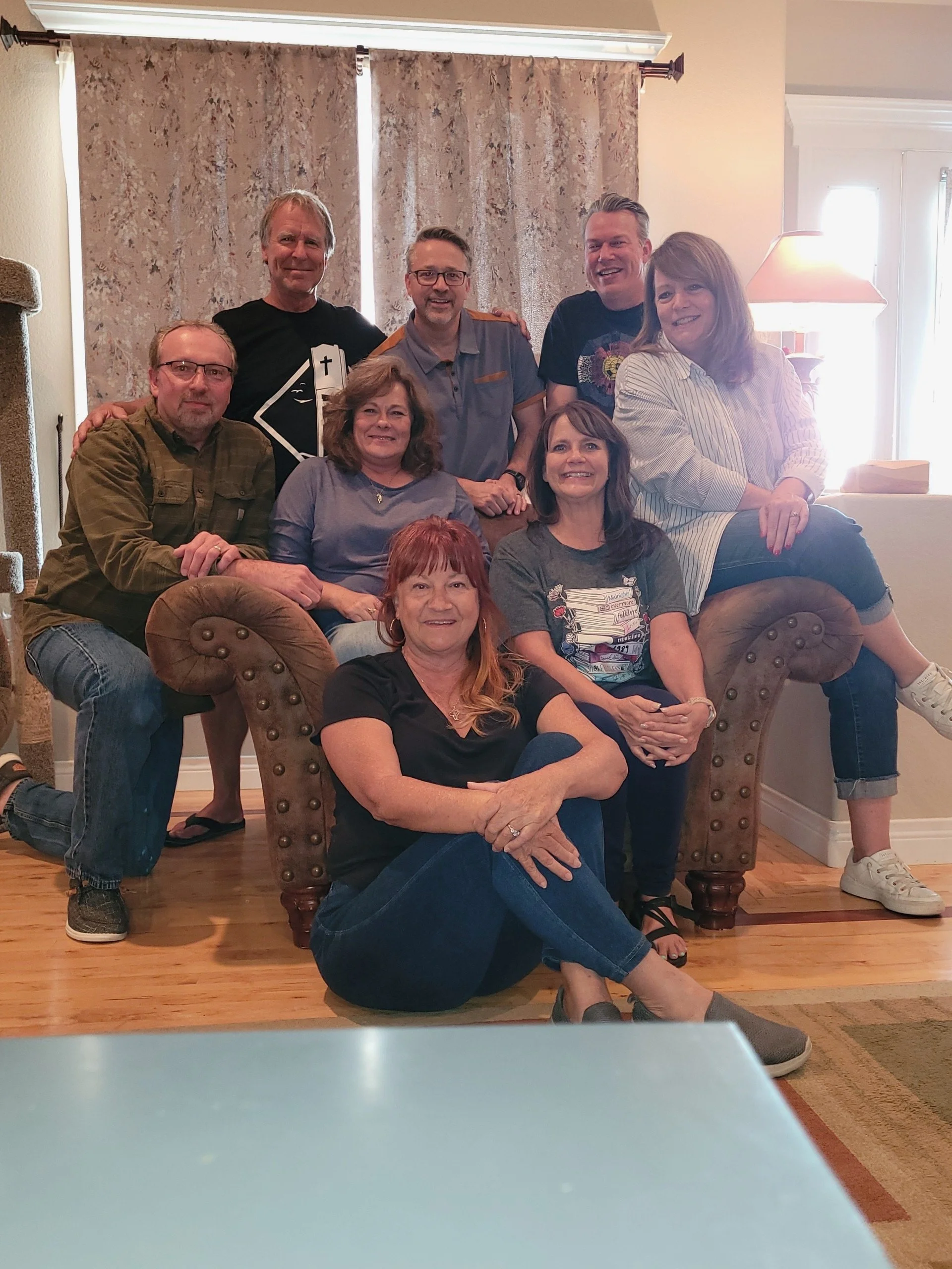 Two men are engaged in a playful lightsaber duel on a stage with red lighting. One man is holding a pink lightsaber and the other a blue lightsaber, with various musical equipment in the background.