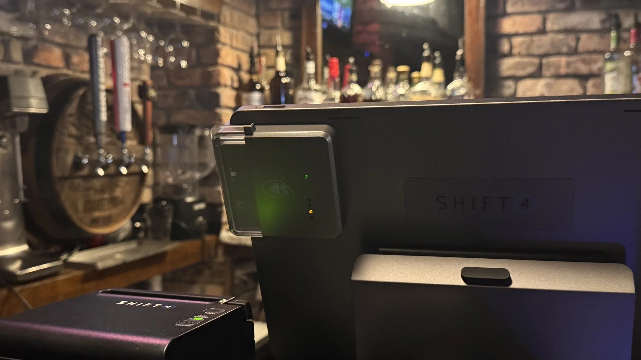 Back of SkyTab terminal and receipt printer, showing Shift4 branding in a bar setting.