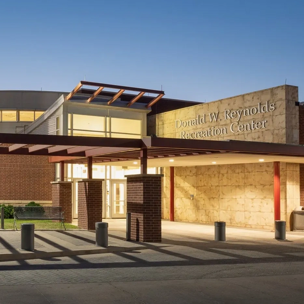 Exterior view of Donald W. Reynolds Recreation Center with entrance illuminated, brick and stone facade, and clear evening sky.