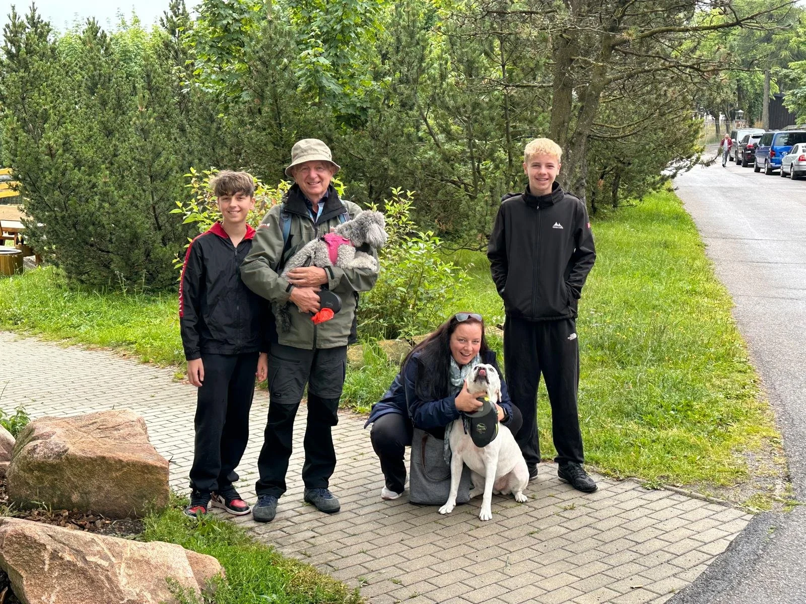 Vier Menschen und zwei Hunde auf einem Spaziergang im Grünen. Drei junge Leute und eine erwachsene Frau, alle lächelnd.
