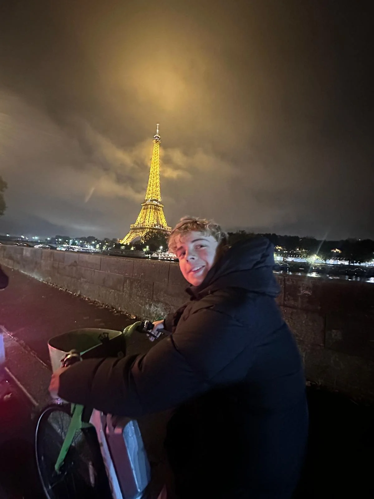 Junge Person fährt mit einem Fahrrad vor der beleuchteten Eiffelturm bei Nacht in Paris, Frankreich.
