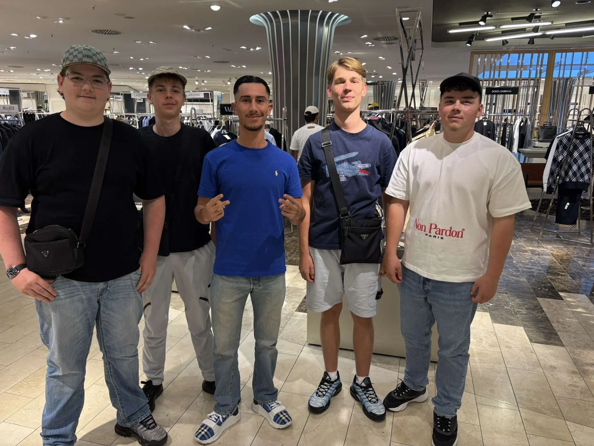 Finn und Freunde aus der Richrath Gruppe treffen Amo im Breuninger in Düsseldorf. Das ist das letzte Bild von Finn. Fünf junge Männer stehen im Einkaufszentrum vor Kleidungsgeschäften.