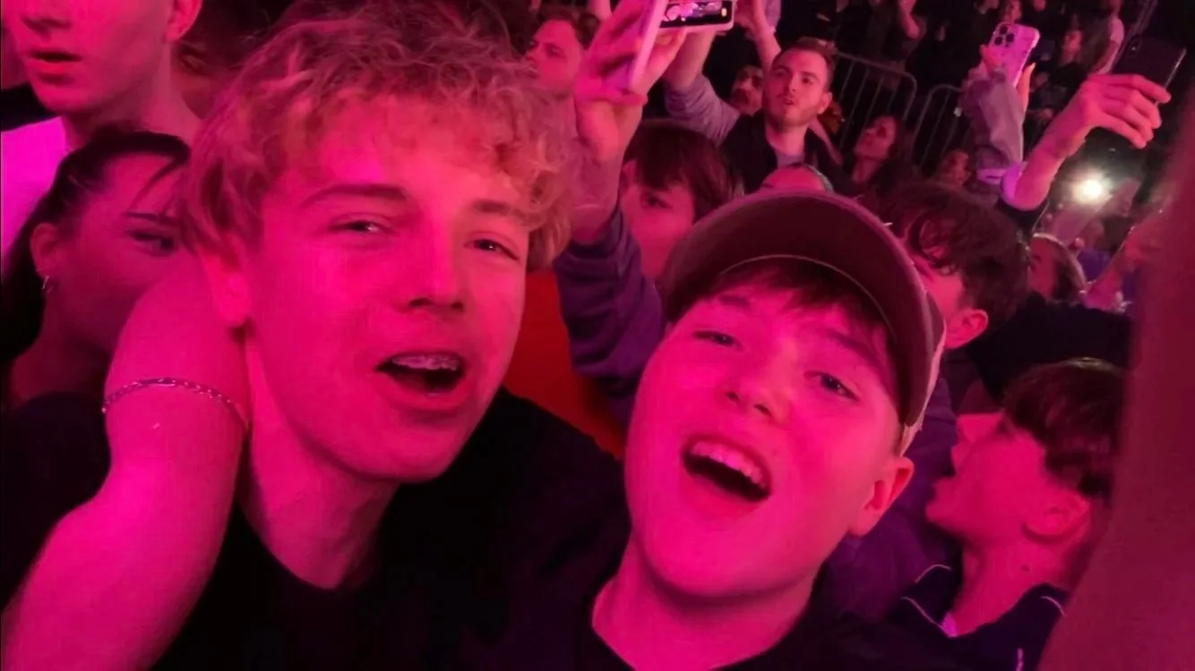Finn und Lance beim Luciano Konzert in Köln 2024. Zwei junge Männer feiern bei einem Konzert mit pinker Beleuchtung, umgeben von anderen Menschen, einige halten Handys hoch.