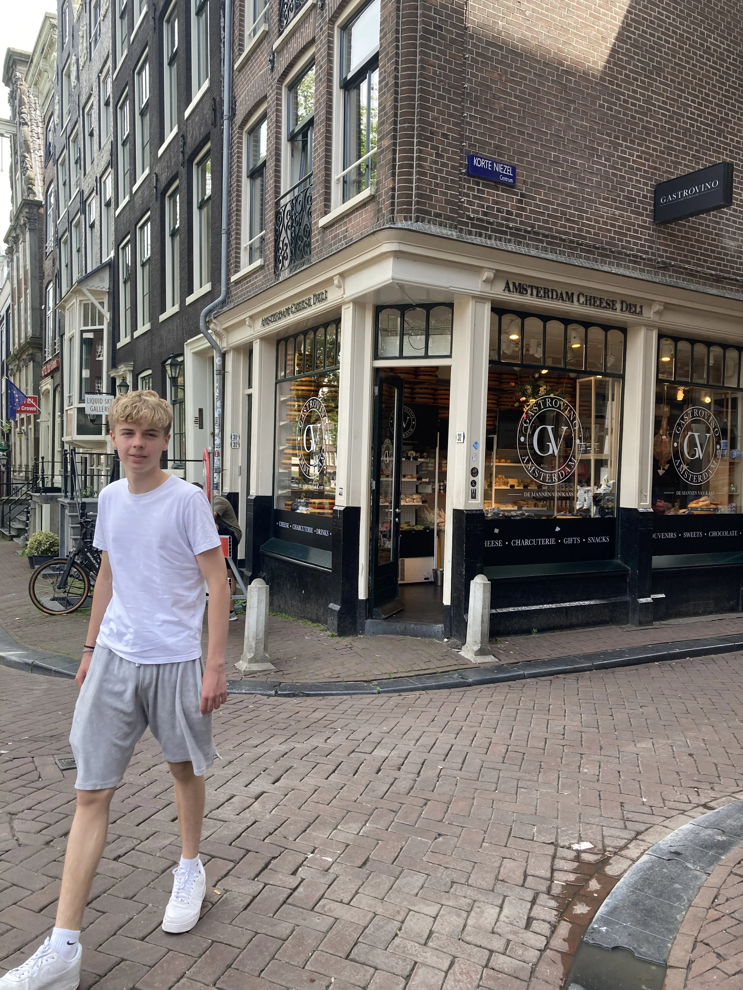 Junge in weißem T-Shirt und grauen Shorts geht an einer Ecke eines Geschäfts in einer Straßenkreuzung vorbei.