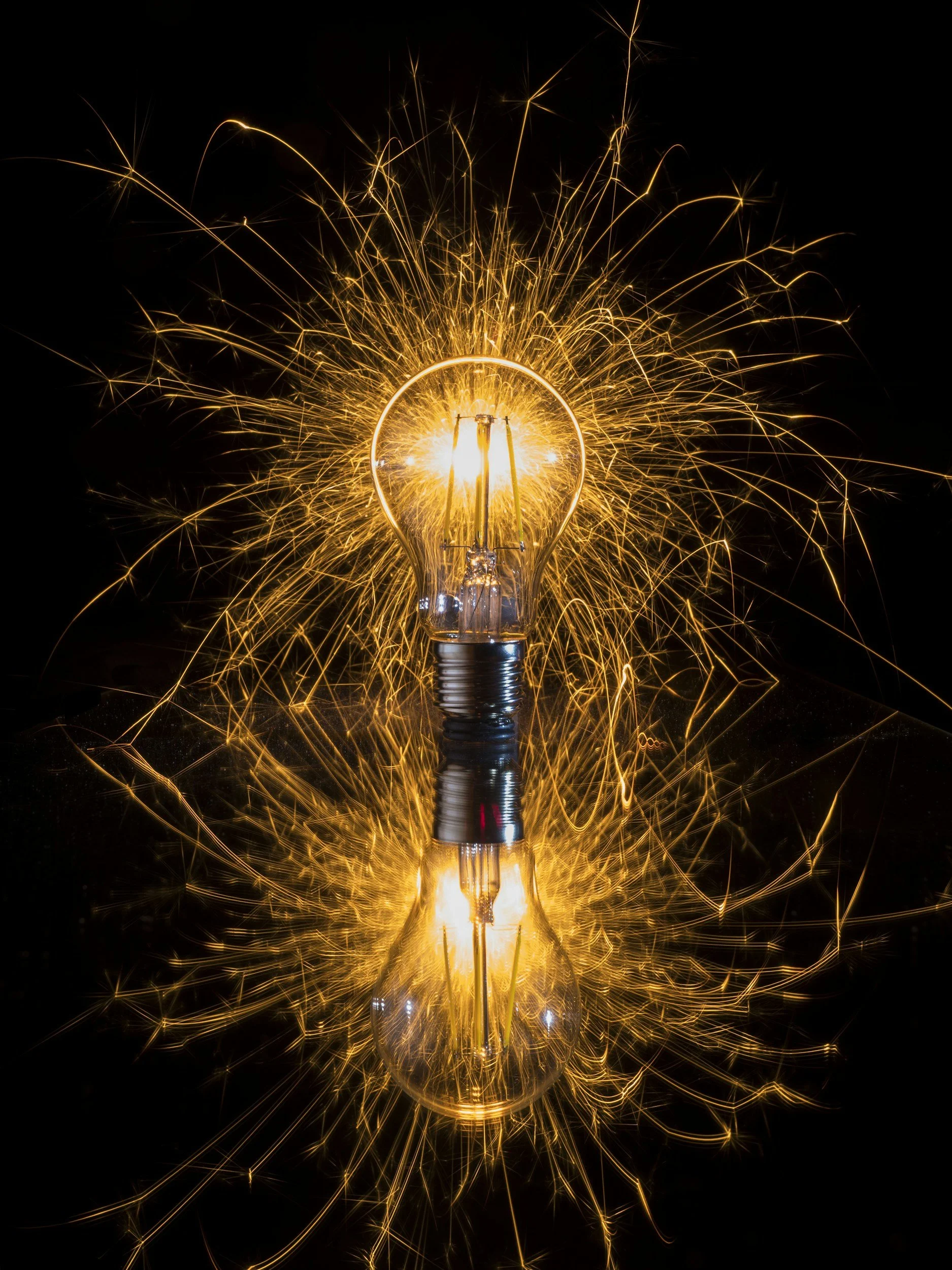 Light bulb surrounded by sparks with reflections on a shiny surface.