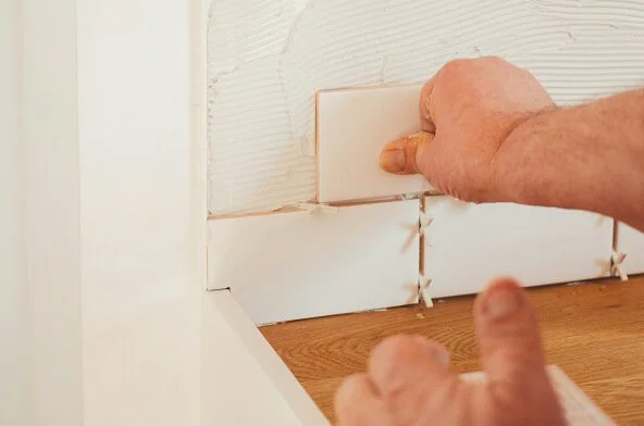 Close-up of person installing or removing a backsplash tile in a kitchen, with a hand gripping a tile and a hand pointing near the tile.